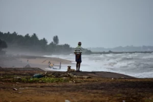 A man and his dog standing by the beach during a storm.
